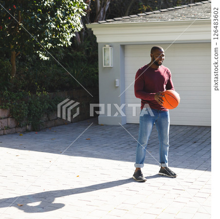 Holding basketball in driveway, man playing outside on sunny day, copy space 126483602