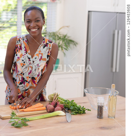 African American woman chopping vegetables in kitchen, smiling and enjoying cooking African American woman chopping vegetables in kitchen, smiling and enjoying cooking 126483608