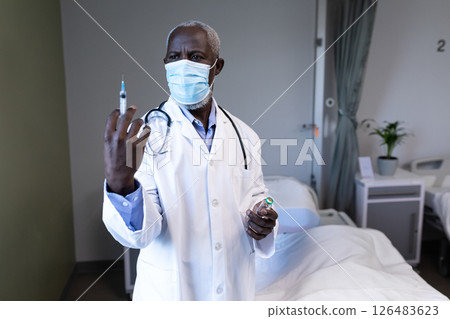 Doctor in white coat preparing syringe in hospital room, focused on task 126483623