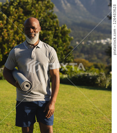 Smiling man holding yoga mat outdoors, enjoying peaceful morning exercise routine 126483628