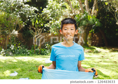 Asian boy volunteering outdoors, holding trash bag and smiling in sunny park 126483633
