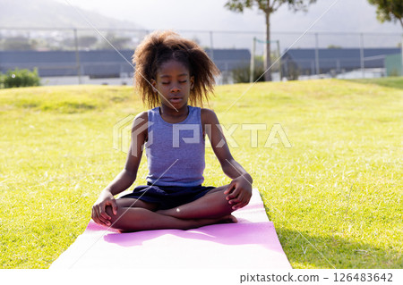 Young girl meditating on yoga mat outdoors, focusing on relaxation and mindfulness 126483642