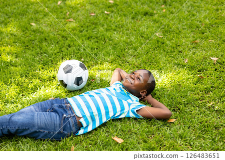 On grass, African American child smiling with soccer ball, relaxing outdoors On grass, African American child smiling with soccer ball, relaxing outdoors 126483651