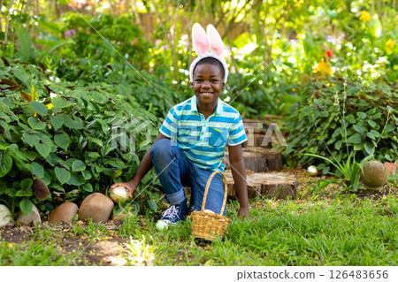 Smiling boy wearing bunny ears collecting Easter eggs in garden Smiling boy wearing bunny ears collecting Easter eggs in garden 126483656