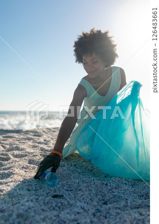 Woman cleaning beach, collecting plastic waste with blue bag under sunny sky 126483661