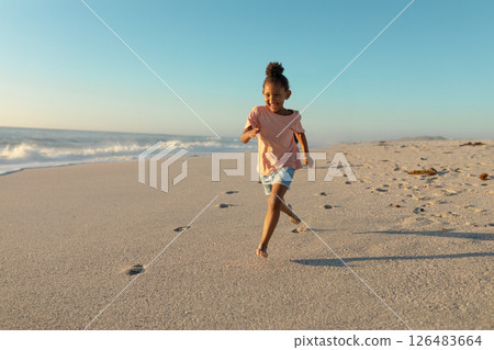 Joyful girl running barefoot on sandy beach, enjoying sunny day by ocean, copy space 126483664