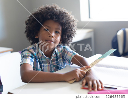 In school, young boy holding ruler at desk, looking confidently at camera 126483665