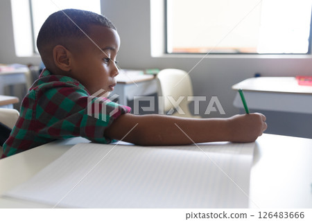 In school, young boy writing in notebook, concentrating in classroom In school, young boy writing in notebook, concentrating in classroom 126483666