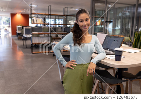 Confident woman standing in modern office, smiling near laptop and coffee cup, copy space 126483675