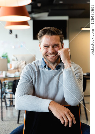 Smiling man in office leaning on chair, looking confident and approachable Smiling man in office leaning on chair, looking confident and approachable 126483692