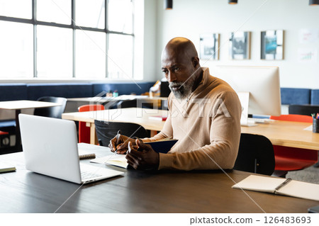 Focused African American man taking notes while working on laptop in modern office 126483693