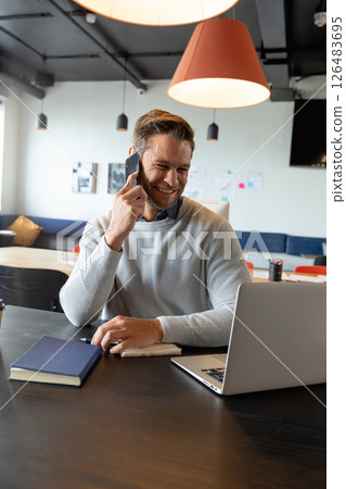 Smiling man in office using smartphone and laptop for business communication Smiling man in office using smartphone and laptop for business communication 126483695