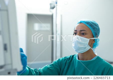 Healthcare professional in scrubs and mask operating medical equipment in hospital, copy space 126483713