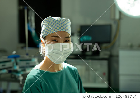 Asian female surgeon wearing mask and cap smiling confidently in operating room 126483714