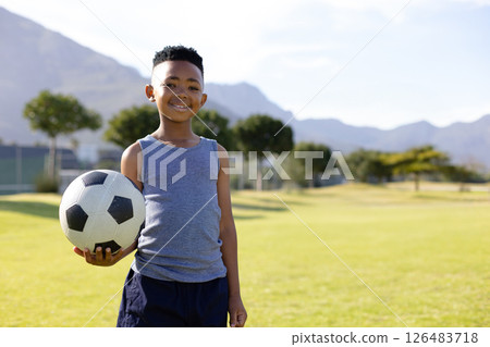 Smiling boy holding soccer ball on school field with mountains in background, copy space 126483718