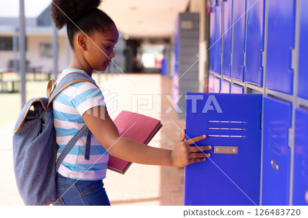 Student opening locker at school, holding book and wearing backpack Student opening locker at school, holding book and wearing backpack 126483720