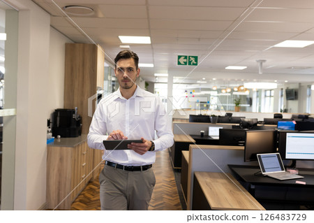 Businessman walking in modern office holding tablet, focused on work, copy space 126483729