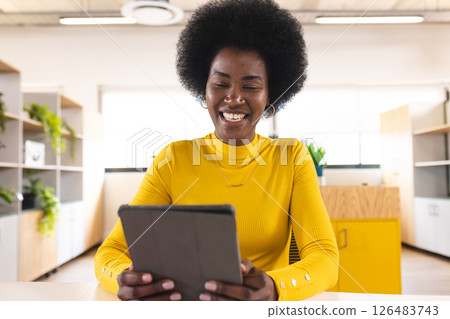 Smiling woman in yellow sweater using tablet in modern office environment 126483743