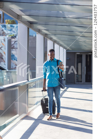 Businessman walking with suitcase and smartphone in modern airport walkway 126483757
