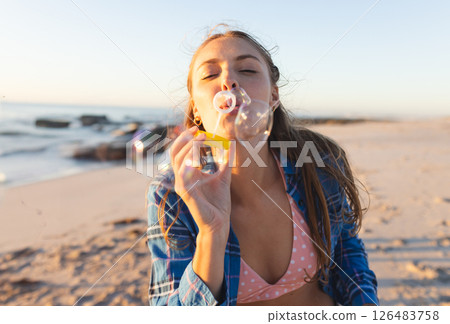 Young woman blowing bubbles on beach, enjoying sunset and ocean breeze 126483758