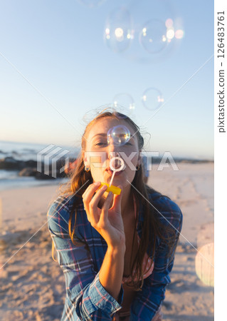 Young woman blowing bubbles on beach at sunset, enjoying carefree moment 126483761