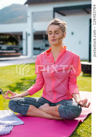 Woman meditating outdoors on yoga mat, enjoying peaceful moment in garden 126483764