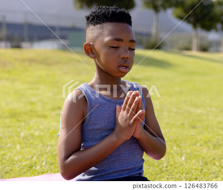 Young boy meditating outdoors on grass, focusing with hands in prayer position 126483766