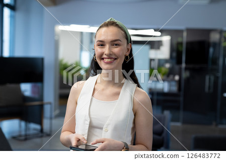 Holding smartphone in office, smiling woman looking confident and approachable 126483772