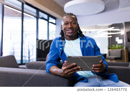 Smiling man using tablet on sofa in modern office, enjoying technology 126483778