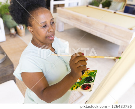 African American woman painting on canvas at home, expressing creativity and focus 126483786
