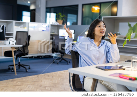 Asian woman in office talking on smartphone, gesturing with hand, looking engaged, copy space Asian woman in office talking on smartphone, gesturing with hand, looking engaged, copy space 126483790