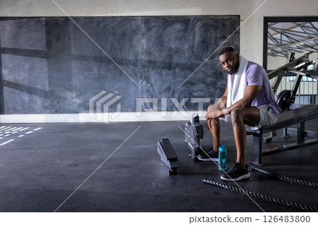 African American man resting on gym bench with towel and water bottle, copy space 126483800