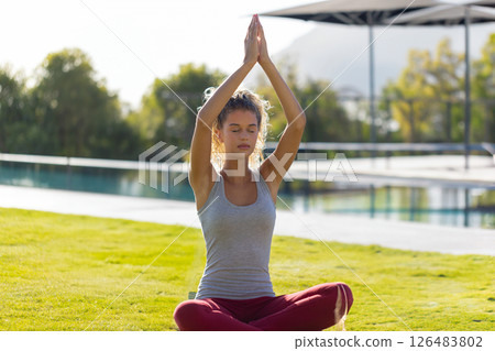 Young woman meditating by pool, practicing yoga with serene expression outdoors Young woman meditating by pool, practicing yoga with serene expression outdoors 126483802