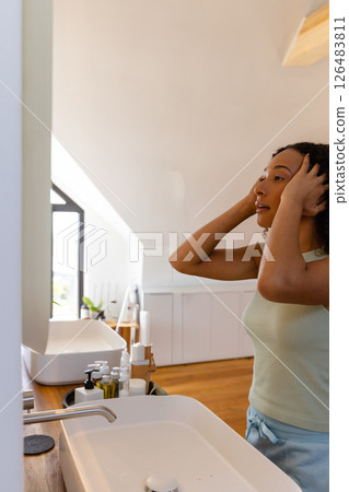 Woman in bathroom adjusting hair in mirror, preparing for day at home 126483811