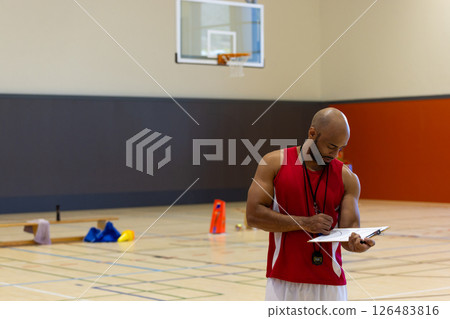 Basketball coach in gym writing on clipboard, planning training session, copy space Basketball coach in gym writing on clipboard, planning training session, copy space 126483816