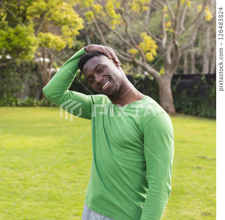 Man in green shirt stretching neck in sunny park, smiling and enjoying nature 126483824