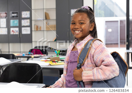 Smiling African American girl with backpack standing in classroom, ready for school, copy space Smiling African American girl with backpack standing in classroom, ready for school, copy space 126483834