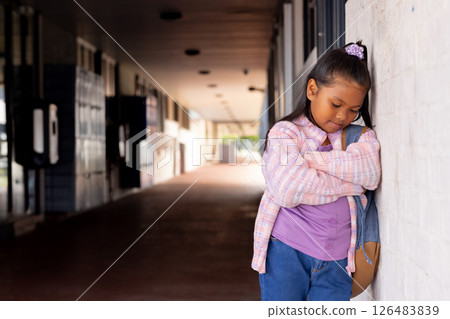 Young girl leaning against school wall, looking thoughtful in hallway, copy space 126483839