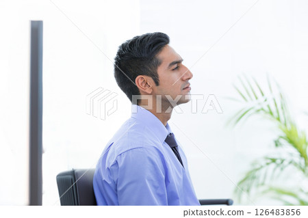 Businessman in blue shirt relaxing at office desk, taking deep breath Businessman in blue shirt relaxing at office desk, taking deep breath 126483856