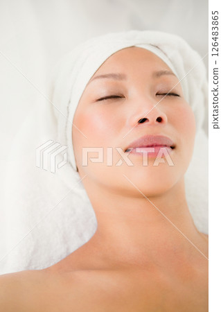 Receiving facial treatment, serene asian woman with towel wrapped head relaxing at spa 126483865