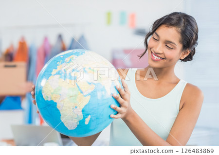Smiling woman holding globe in office, exploring global business opportunities Smiling woman holding globe in office, exploring global business opportunities 126483869