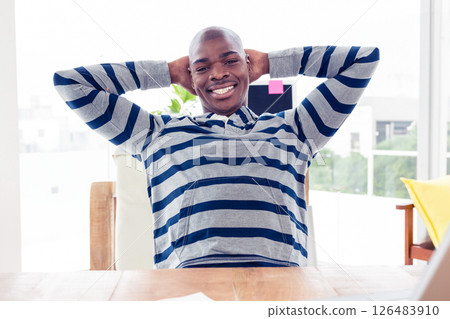Smiling man in striped hoodie relaxing at office desk, feeling content 126483910