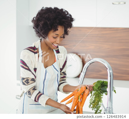 Woman washing fresh carrots in kitchen, smiling and enjoying cooking at home 126483914