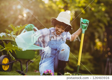 Woman gardening, wearing hat and gloves, watering plants with joy in backyard Woman gardening, wearing hat and gloves, watering plants with joy in backyard 126483916