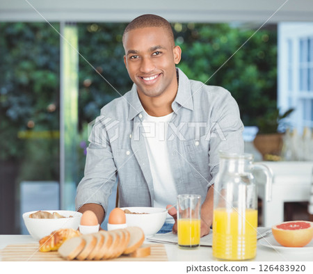Smiling African American man preparing breakfast with fresh juice and bread in modern kitchen Smiling African American man preparing breakfast with fresh juice and bread in modern kitchen 126483920