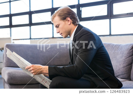 Businessman in suit reading newspaper on sofa in modern office lounge 126483923