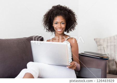 Smiling woman using laptop on couch at home, relaxing and enjoying leisure time 126483929