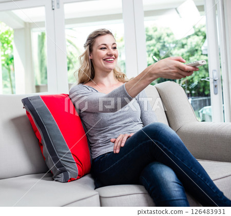 Smiling woman relaxing on sofa, using remote control at home, enjoying leisure time Smiling woman relaxing on sofa, using remote control at home, enjoying leisure time 126483931