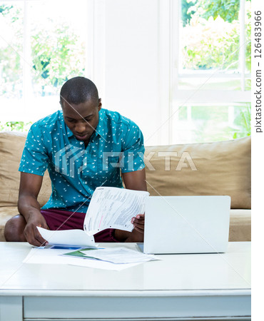 African American man reviewing documents with laptop at home, concentrating on work African American man reviewing documents with laptop at home, concentrating on work 126483966