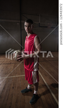Young man in red jersey holding basketball confidently on indoor court 126483972